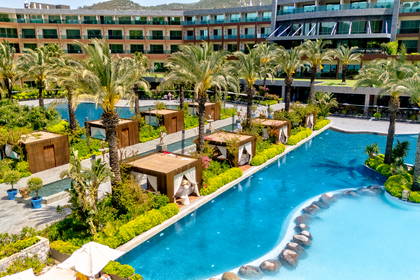 Hotel z basenem, palmami i altanami widziany z góry.