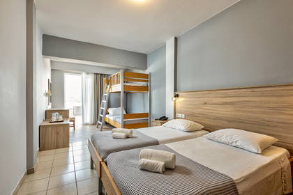 Pokój hotelowy z dwoma łóżkami, łóżkiem piętrowym i biurkiem.