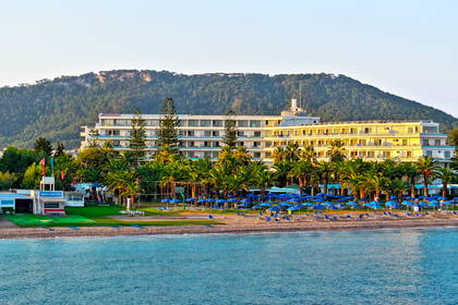 Hotel przy plaży z parasolami i palmami. W tle widoczna góra.