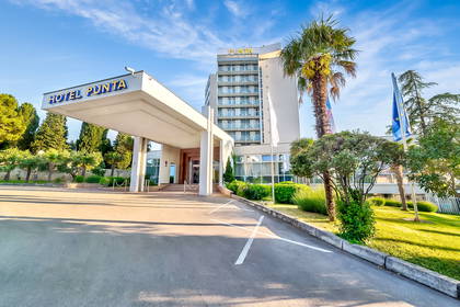 Hotel Punta z parkingiem otoczony zielenią w słoneczny dzień.