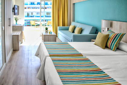 Jasny pokój hotelowy z dwoma łóżkami, sofą i balkonem.