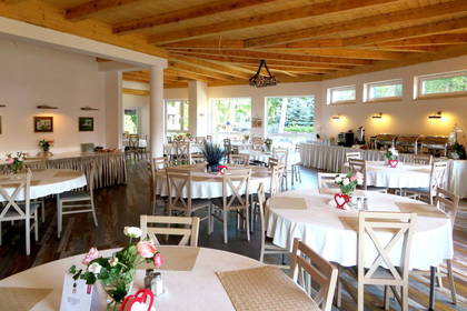 Jasne wnętrze restauracji. Drewniany sufit, okrągłe stoły z białymi obrusami.