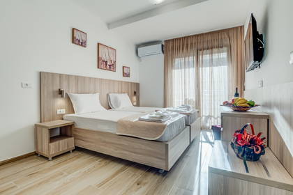 Jasny pokój hotelowy z dwoma łóżkami, stolikami nocnymi i koszem owoców.