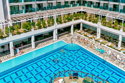 Widok z góry na basen hotelowy z pływającymi osobami i leżakami.