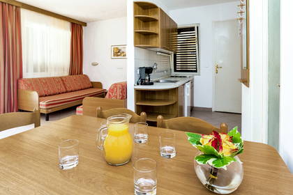 Wnętrze apartamentu łączące salon z czerwoną kanapą, aneks kuchenny oraz jadalnię.