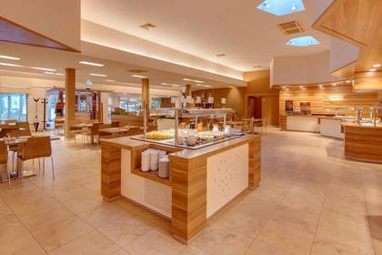 Jasna restauracja hotelowa z bufetem i stolikami.