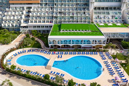 Widok z lotu ptaka na duży hotel z basenem w kształcie ósemki, który otaczają niebieskie leżaki.