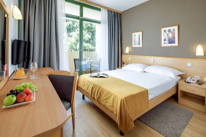 Jasny pokój hotelowy z podwójnym łóżkiem, biurkiem i umeblowanym balkonem.