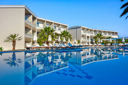 Kompleks hotelowy z basenem, leżakami i palmami.