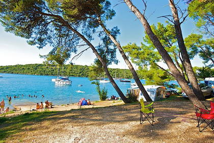 Plaża z wypoczywającymi ludźmi. W tle jachty i zalesione wzgórza.