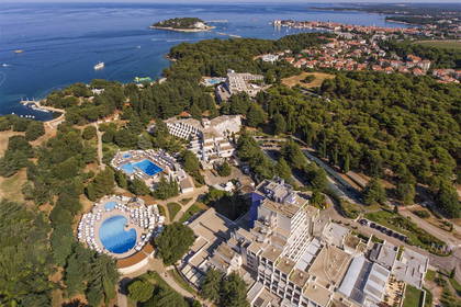 Zdjęcie lotnicze hotelu z basenami, morza i miasta w tle.