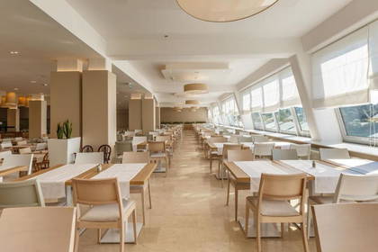 Jasne wnętrze restauracji z rzędami nakrytych stołów i dużymi oknami.
