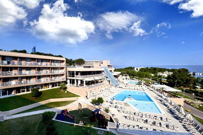 Hotel z basenem i placem zabaw, w tle morze.