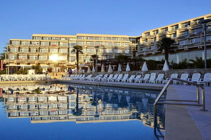 Hotel z basenem i leżakami w słoneczny dzień.