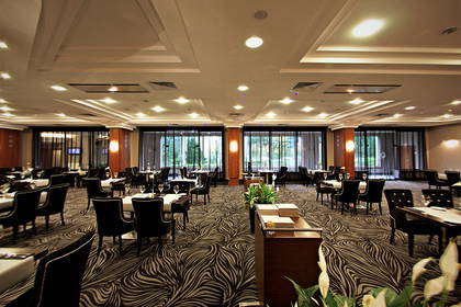 Sala restauracyjna z nakrytymi stołami i wzorzystą wykładziną podłogową.