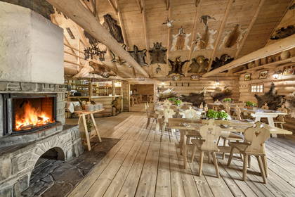 Drewniane wnętrze restauracji w stylu góralskim. W środku kominek i skóry zwierząt.
