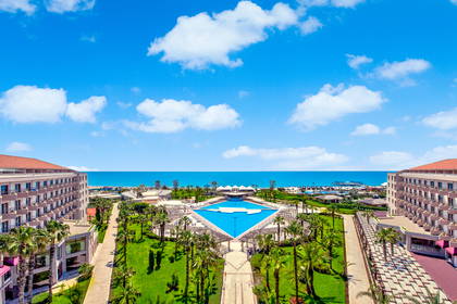 Hotel z basenem i palmami. W tle widok na morze.