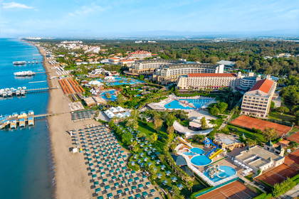 Widok z lotu ptaka na kurort z basenami, kortami tenisowymi, hotelami i parasolami na plaży.