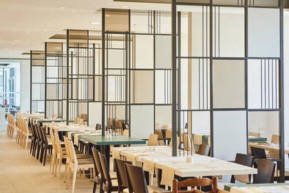 Sala restauracyjna ze stołami i krzesłami oddzielonymi panelami.