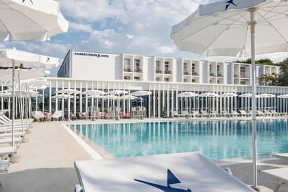 Biały hotel Falkensteiner z basenem i leżakami do opalania.