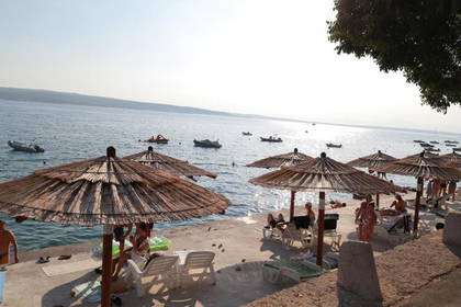 Plaża ze słomianymi parasolami, leżakami i łodziami na morzu.