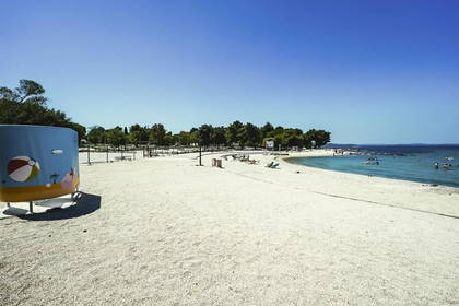 Plaża z białym piaskiem i turkusową wodą pod błękitnym niebem.