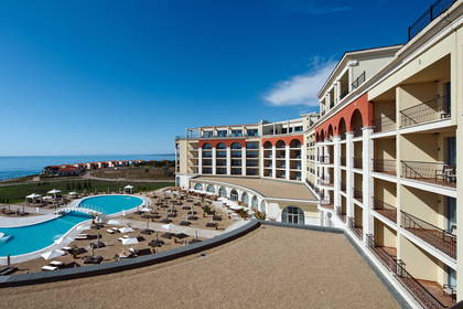 Hotel z basenem, morzem i błękitnym niebem w tle.
