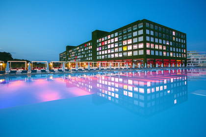 Hotel nocą. Światła budynku odbijają się w basenie.