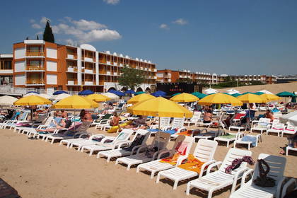 Plaża z leżakami, parasolami i budynkiem hotelu w tle.