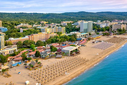 Plaża z parasolami, hotele i zalesione wzgórza w tle, widok z lotu ptaka.