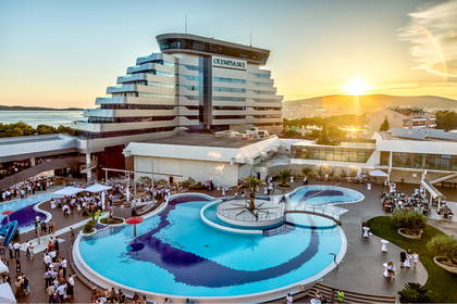 Hotel Olympia Sky z basenem oświetlonym promieniami zachodzącego słońca.