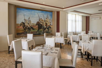Restauracja z białymi krzesłami, stołami i obrazem jeźdźców na ścianie.