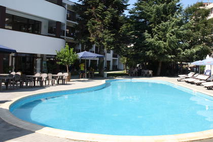 Hotel z basenem, leżakami i stolikami w otoczeniu drzew.