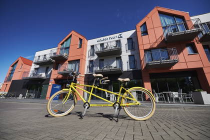 Żółty rower tandem stoi przed budynkiem Golden Tulip.