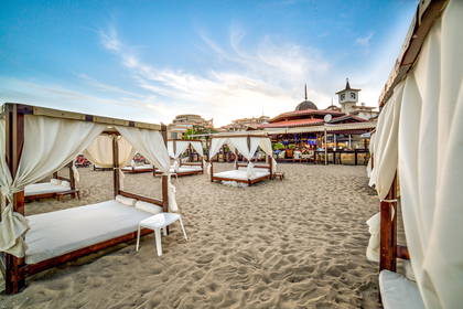 Plaża z baldachimami przeciwsłonecznymi i budynkiem w tle.
