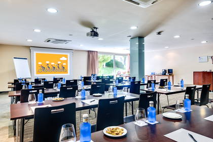 Sala konferencyjna z ekranem projekcyjnym, stołami i krzesłami.