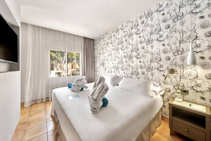 Pokój hotelowy z dużym łóżkiem, szafką nocną i tapetą w kwiaty.