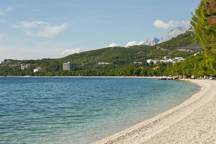 Plaża z białymi kamieniami, morze i góry w tle.