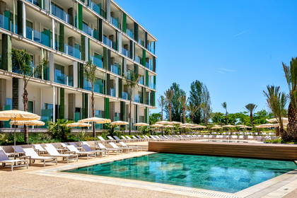 Hotel z basenem i strefą relaksu w słoneczny dzień.