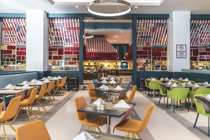 Wnętrze restauracji. Nakryte stoliki i krzesła w kolorach żółtym oraz zielonym.