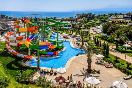 Aquapark z kolorowymi zjeżdżalniami, basenami, leżakami i palmami, widok z góry.