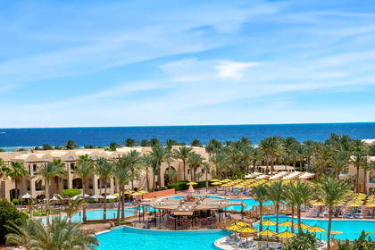 Luksusowy hotel z basenami i palmami. W tle widok na morze.