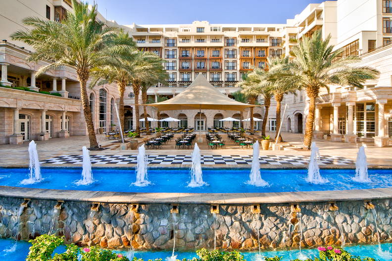 Dziedziniec hotelowy z fontanną i palmami.