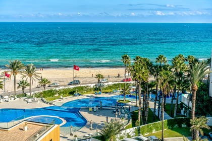 Turkusowe morze, plaża z palmami i baseny hotelowe.