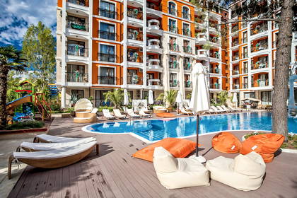 Kompleks hotelowy z basenem, leżakami i placem zabaw dla dzieci.