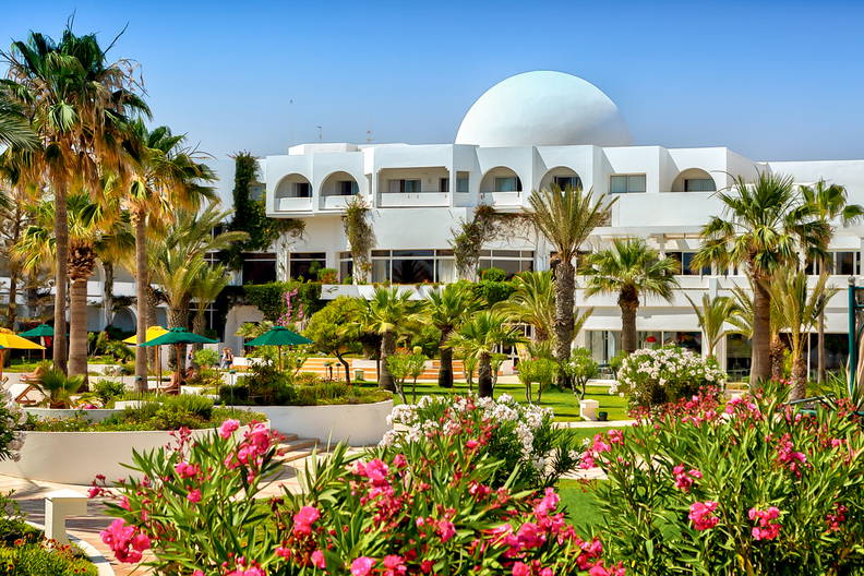 Hotel z białą kopułą otoczony palmami i zielenią.