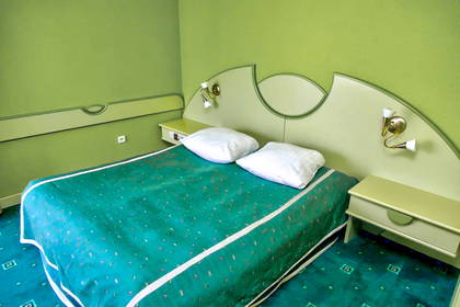 Pokój hotelowy w zielonych odcieniach z dużym łóżkiem.