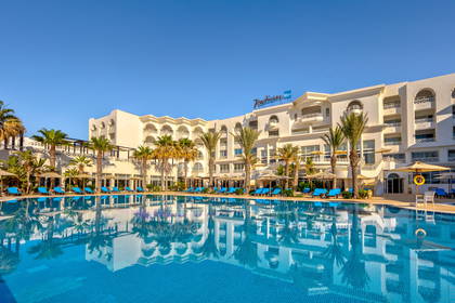 Hotel Radisson Blu z basenem i palmami w słoneczny dzień.