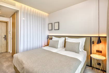 Jasny pokój hotelowy z dużym łóżkiem i stolikiem nocnym.
