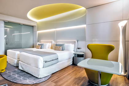 Pokój hotelowy z dwoma łóżkami, nastrojowym oświetleniem i designerskim krzesłem.